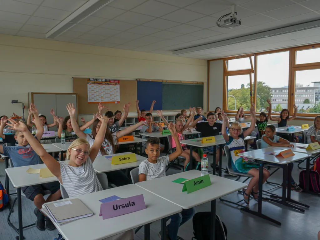 Kinder melden sich mit erhobenen Armen.
